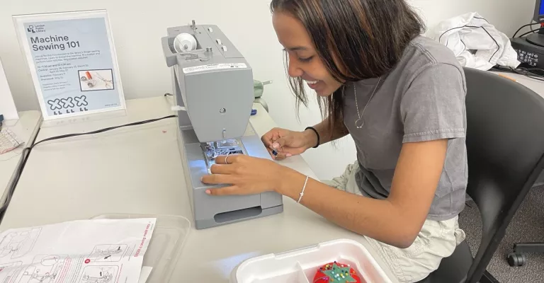 Photo of a young woman using a sewing machine and smiling as she threads the needle.