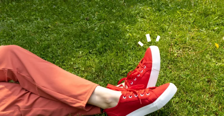 Photo showing someone from the knees down, lying on grass, with legs crossed and wearing red sneakers. Above the sneakers are white line illustrations.