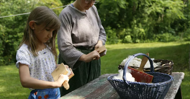 Staff from Fanshawe Pioneer Village dressed in pioneer clothing next to child at a table with baskets