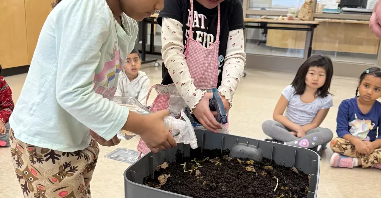 Two children spraying water on seeds they planted