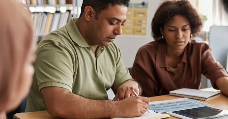 Two people sit at a table looking over documents.