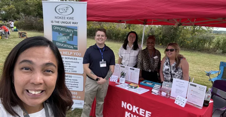 Five adults stand around a table displaying material from Nokee Kwe.
