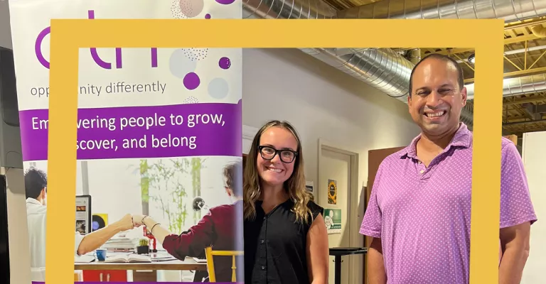 ATN staff stand behind an information table and smile.
