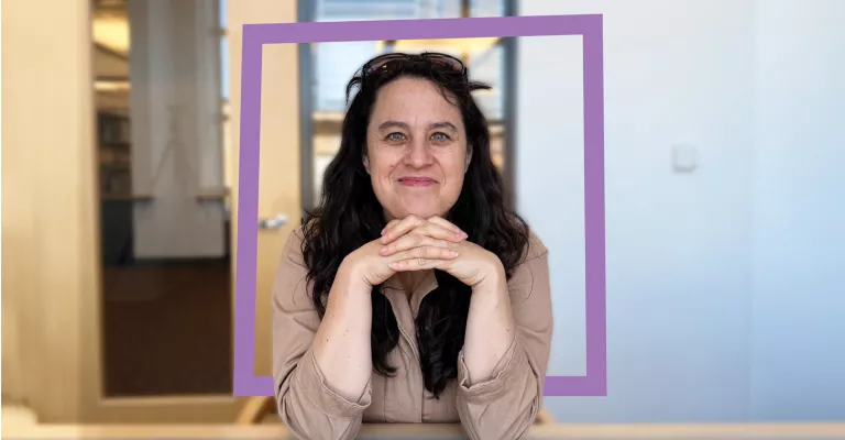 Anna Chatterton leans forward on a table with her elbows, with a purple square graphic behind her.