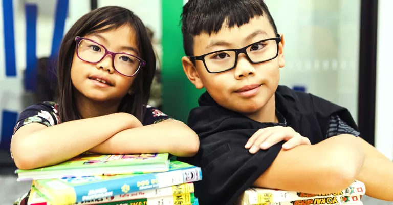 Two children cross their arms on a stack of books