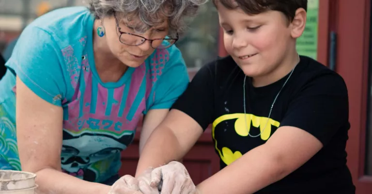 An adult and tween working on a pottery wheel 