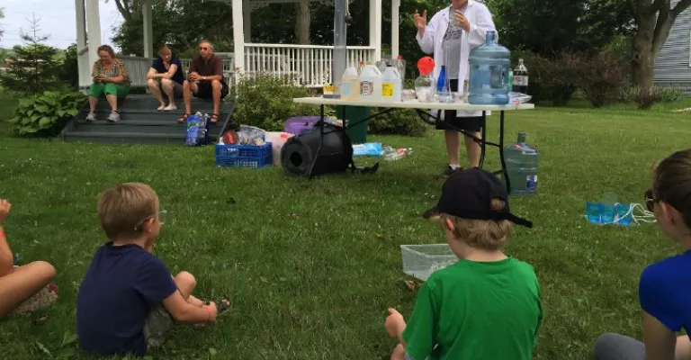 Craig the Science guy in a white doctor's coat teaching children on the front lawn of a house