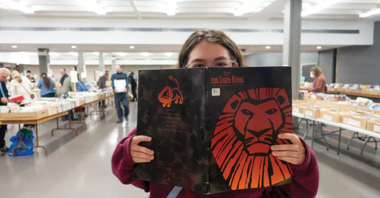 Person holding a copy of The Lion King at a large book sale.