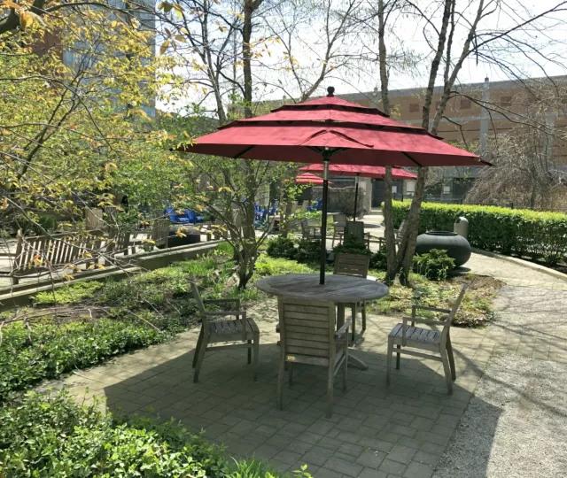 A photo of a wooden table and chairs with a red umbrella on top in the Rotary Reading Garden.