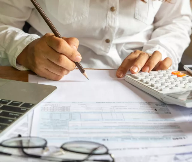 Woman in front of a laptop with a calculator filling out tax forms
