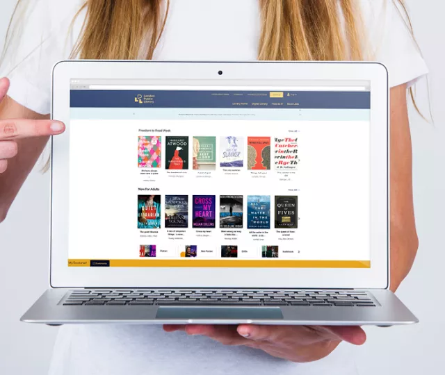  A woman holds a laptop, pointing at the screen which displays London Public Library's catalogue.