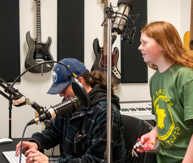 Isaak stands next to his dad in front of a computer in the Central Library recording studio.