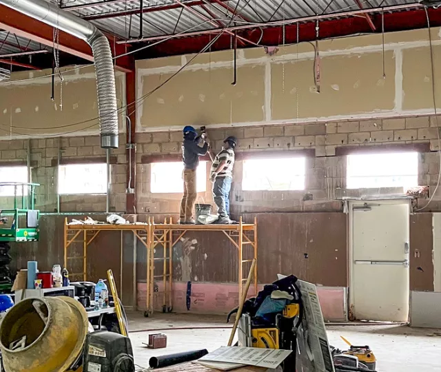 Four construction workers on scaffolding installing windows in a Library renovation.