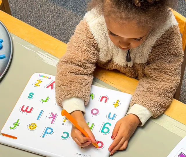 A young girl sits at a table with books, letters, and literacy activities.