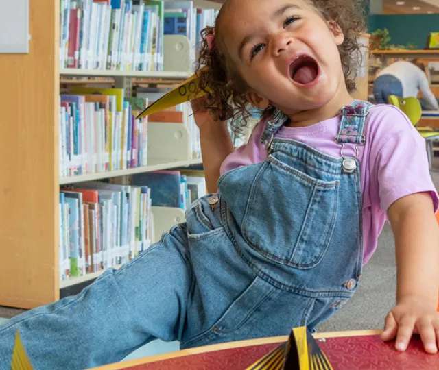 Young girl plays with a paper airplane while excitedly shouting