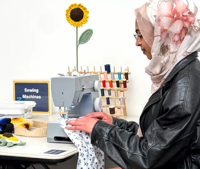 Nourhan sitting and sewing at the Library sewing machine in the Labs