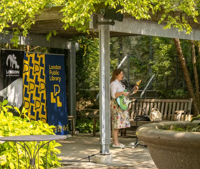 A guitarist plays music in the Rotary Reading Garden with library banners in the background