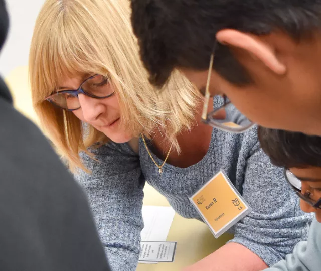 Volunteer woman leaning over table surrounded by kids. 