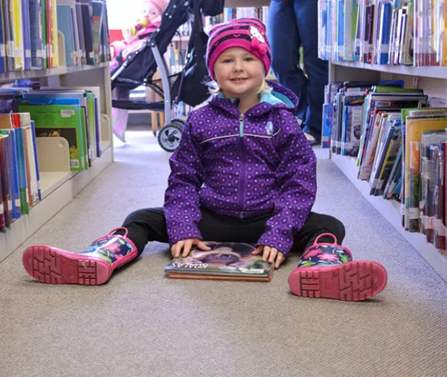 A young girl sits with a book on the carpet in Pond Mills Branch Library.