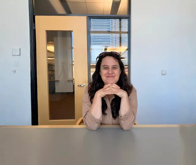 Writer In Residence Anna Chatterton smiles and leans forward on a table.