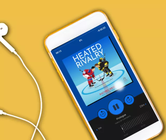 A smart phone with headphone plugged in on a yellow background. The screen shows the audiobook of Heated Rivalry playing.
