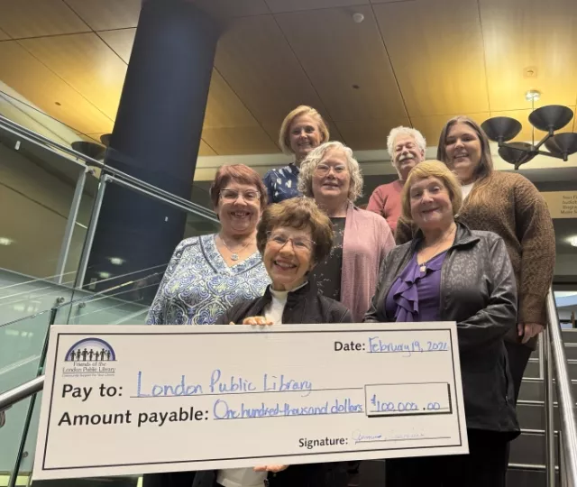 Three members of the Friends executive are joined by four members of the Library board on the stairs at Central Library. Carmen Sprovieri, Friends President stands in front holding a cheque for $100,000 made out to London Public Library.