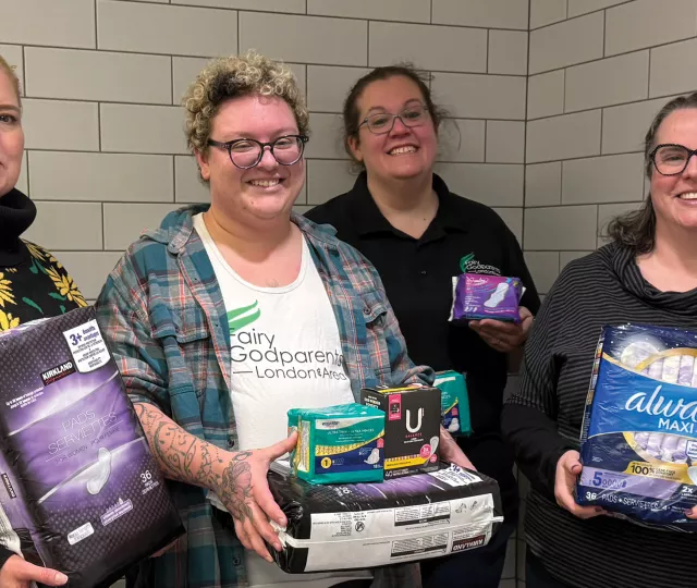 4 people standing in a public washroom holding period products