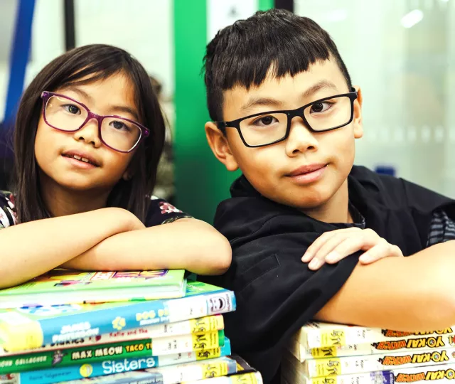 Two children cross their arms on a stack of books