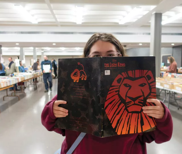 Person holding a copy of The Lion King at a large book sale.