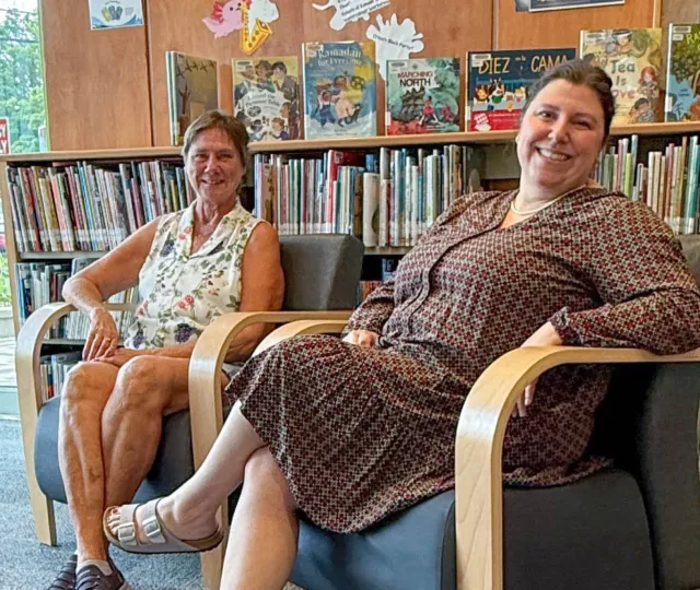 Two smiling women sit on chairs in the children's area of Crouch Branch Library with bookshelves in the background.