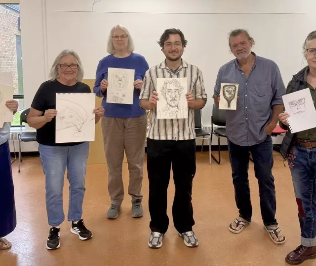 six people stand each holding a self portrait drawing on white paper