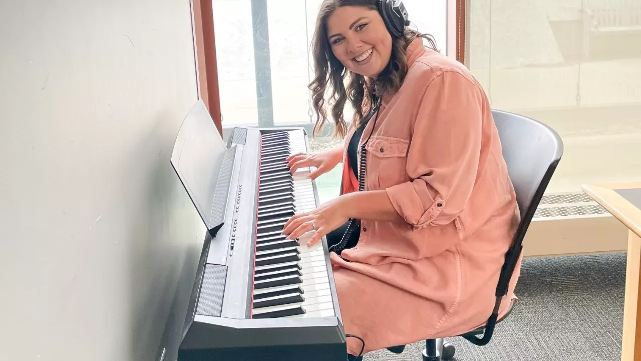 Woman sits at keyboard wearing headphones and with her fingers on the keys. Window in the background.