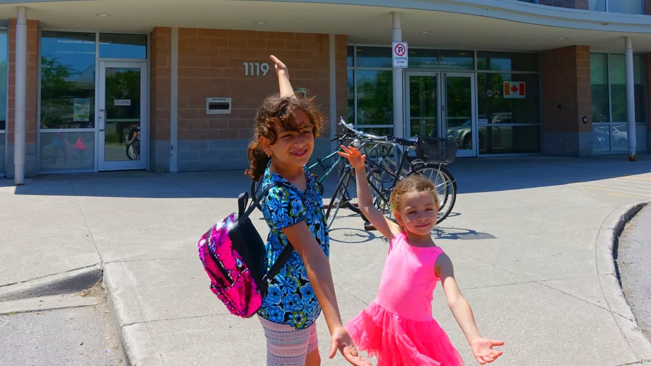 Photo of two young girls standing in front of Jalna Branch library with their arms in the air.