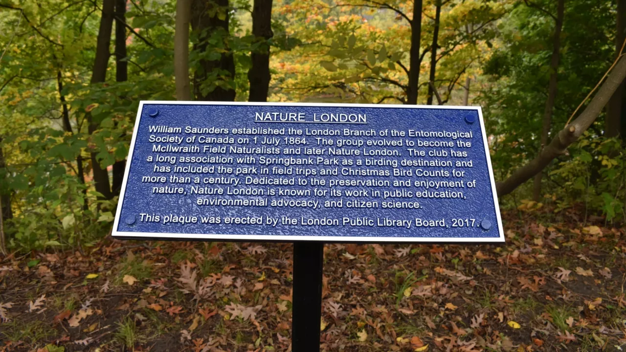A photo of the plaque erected by the Historic Sites Committee in recognition of Nature London. In the background are trees.