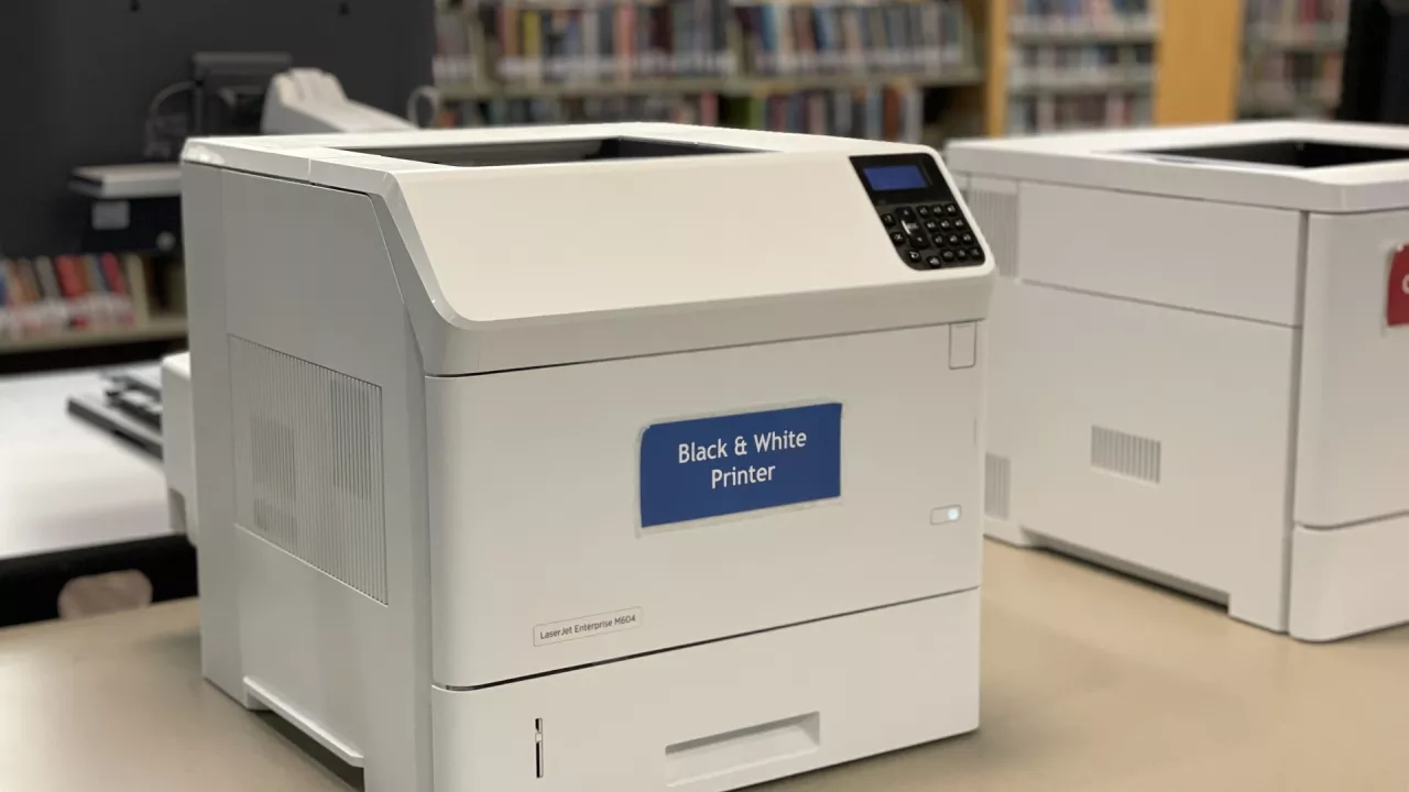 Photo of a black and white printer sitting on a table in the Library.