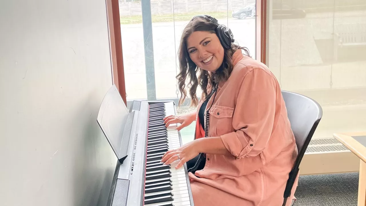Photo of a woman playing a digital piano at the Library. She is wearing headphones and is looking up and smiling.