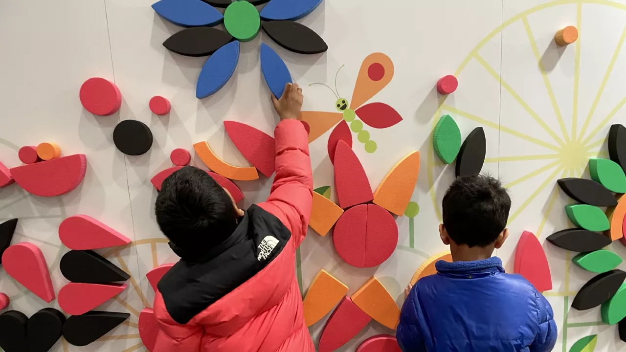 Photo of the back of two boys placing colour foam blocks on the large interactive wall in the Children's Library.