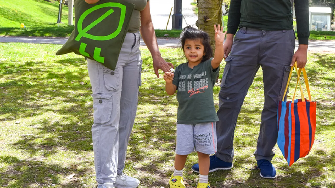 A young family waving at the camera in a field of green grass.