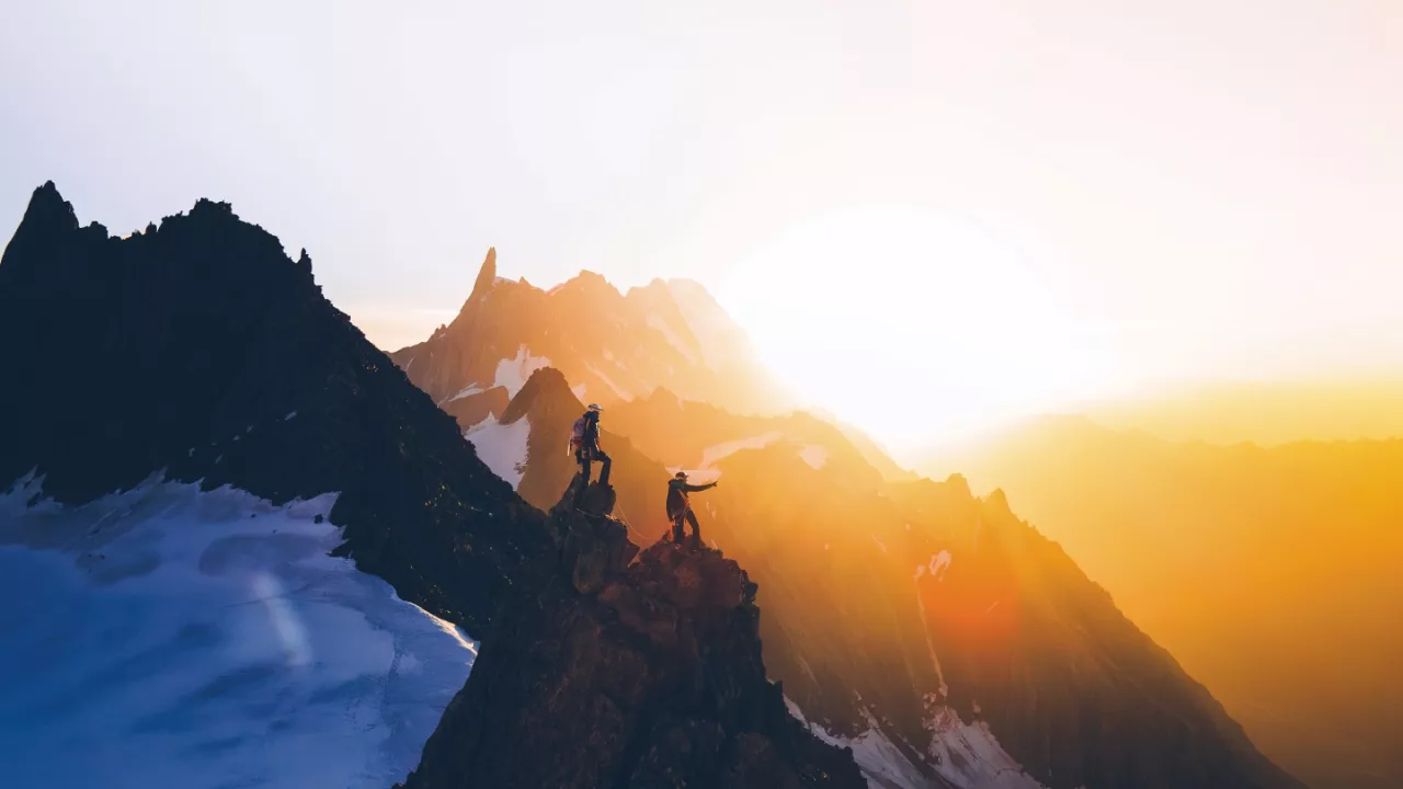 2 Climbers at the top of the French Alps as the sun sets directly behind them.