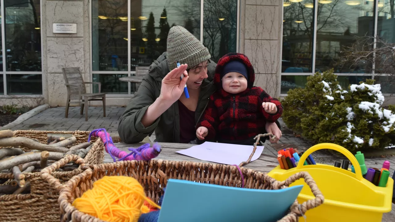 Mother and baby sit at table in the Reading Garden doing crafts.