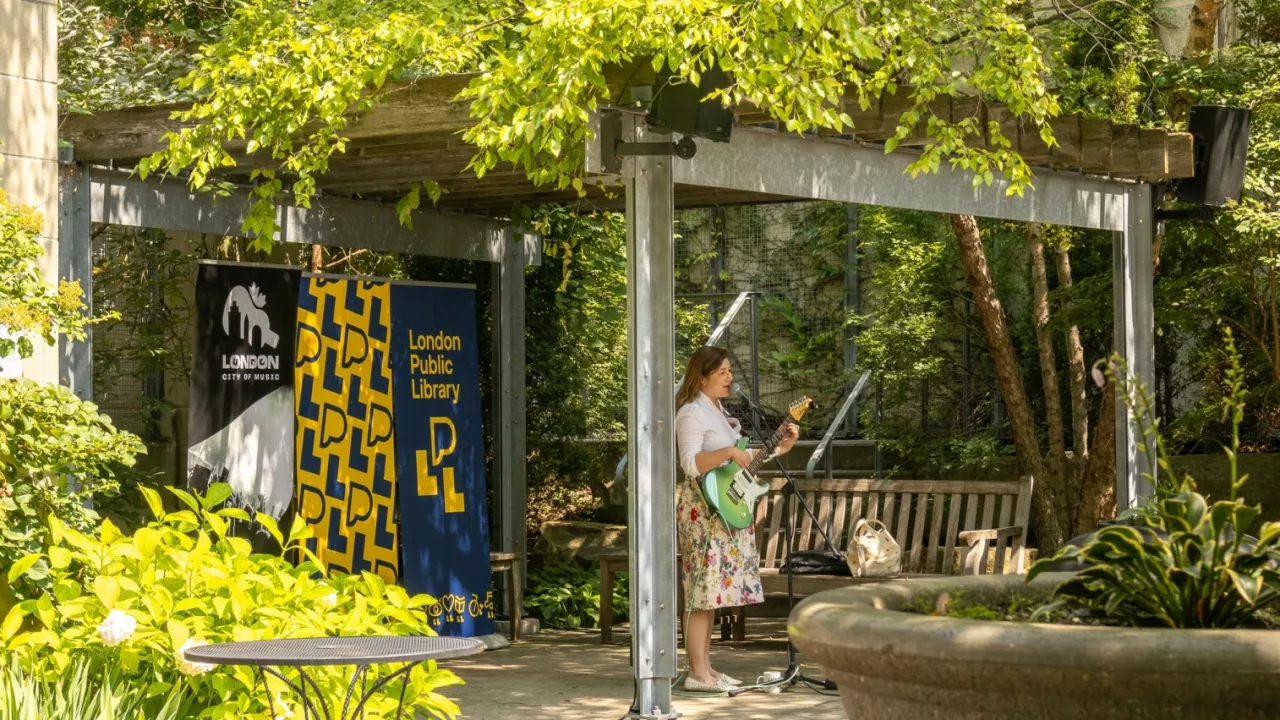 A musician plays guitar in the Reading Garden with Library banners in the background.