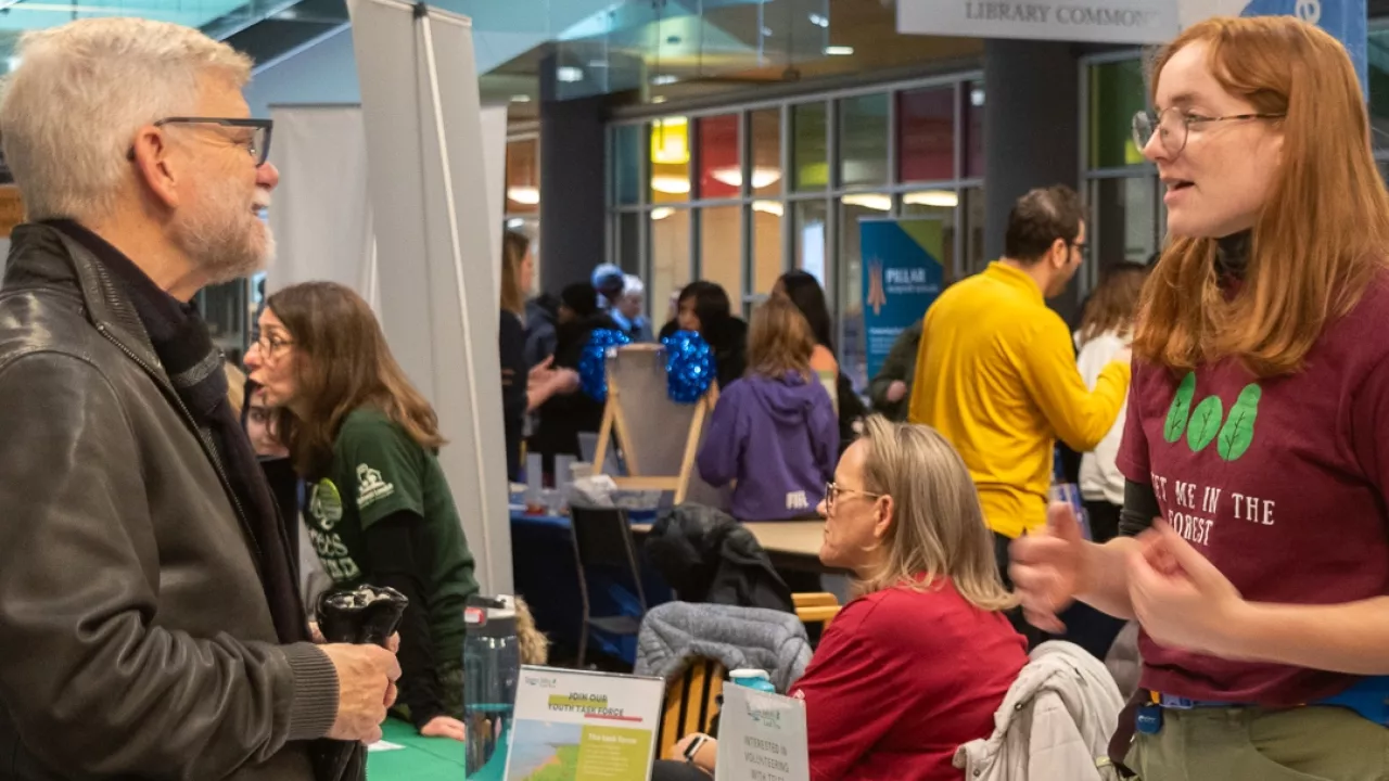 A representative from the organization speaks with a man at the Volunteer Fair Fair at Central Library.