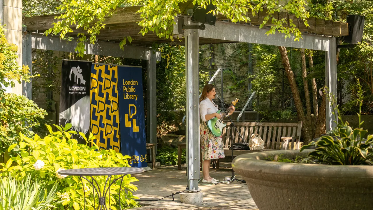 A guitarist plays music in the Rotary Reading Garden with library banners in the background