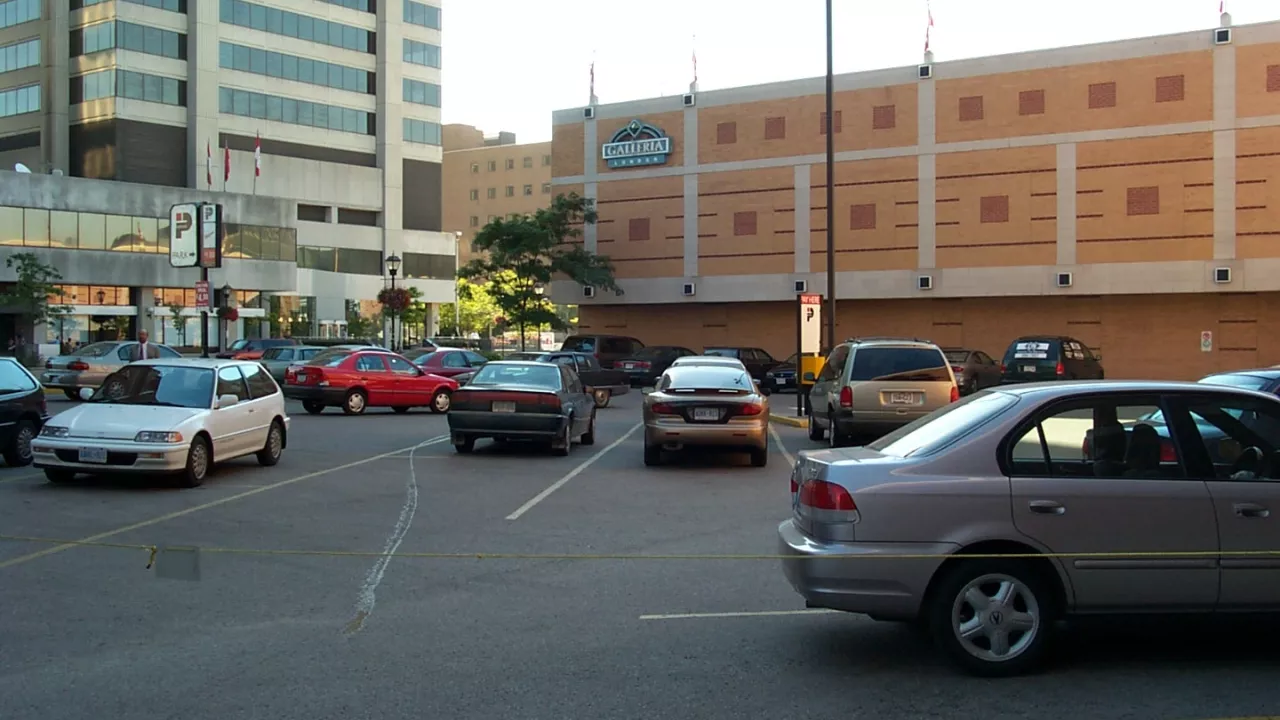 Cars parked in a parking lot on the site of what is now the Reading Garden.  In the background is a sign for the Galleria Mall.