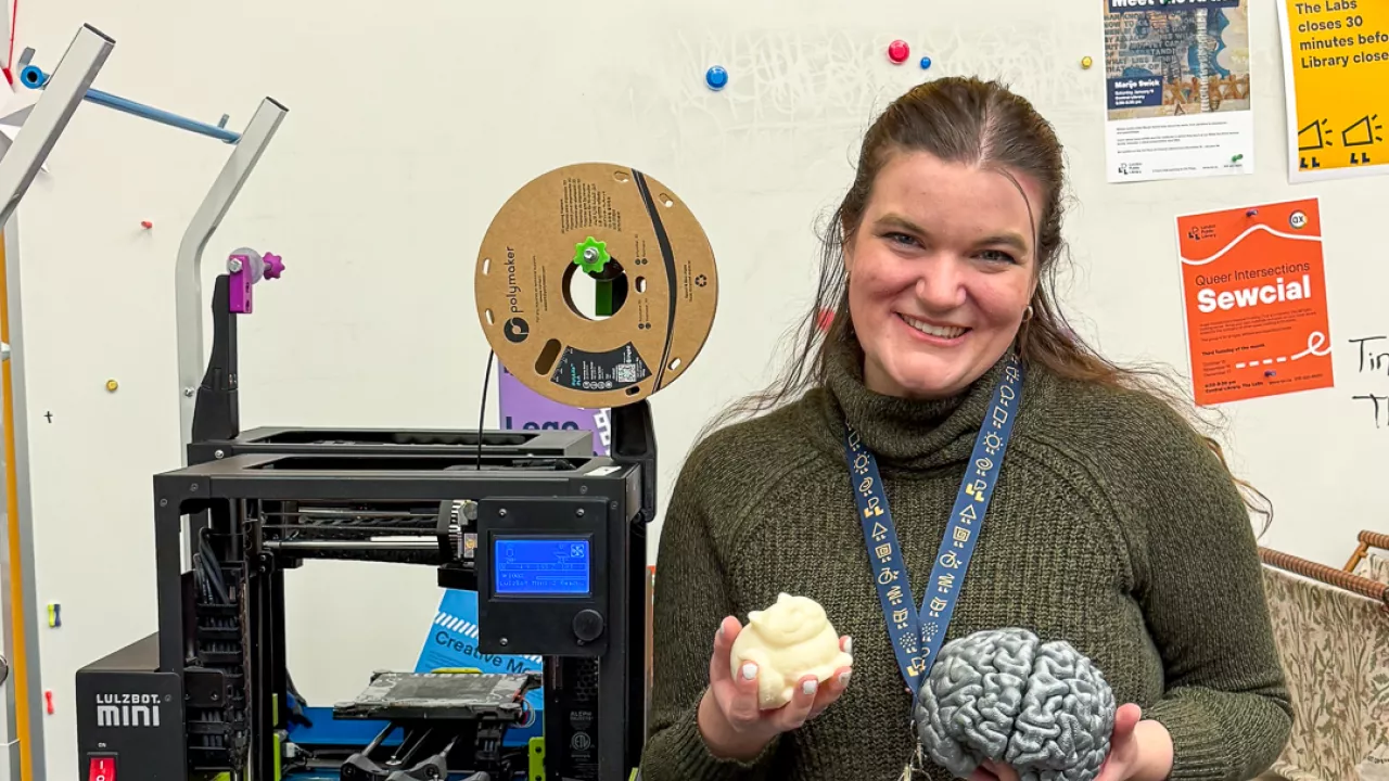 A librarian stands in The Labs at Central Library holding 2 objects that were 3D printed on the 3D printer in The Labs