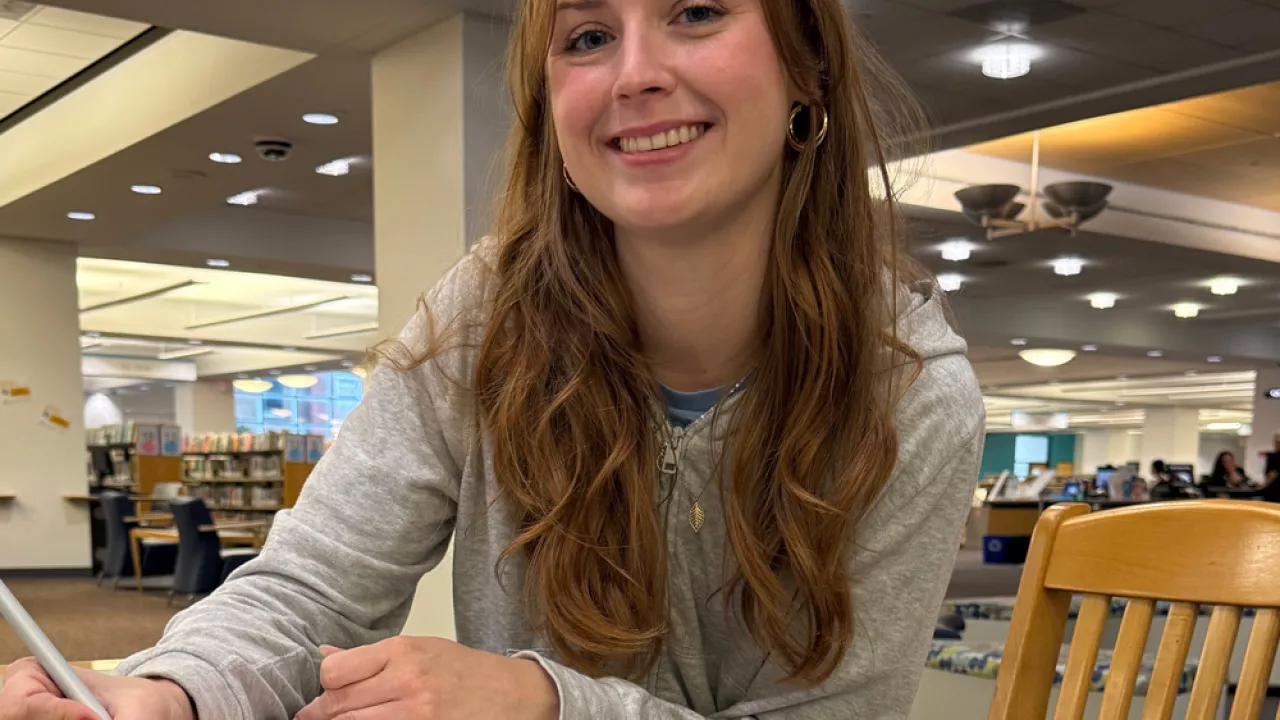 A teenager smiling and looking at the camera while create a bookmark with markers