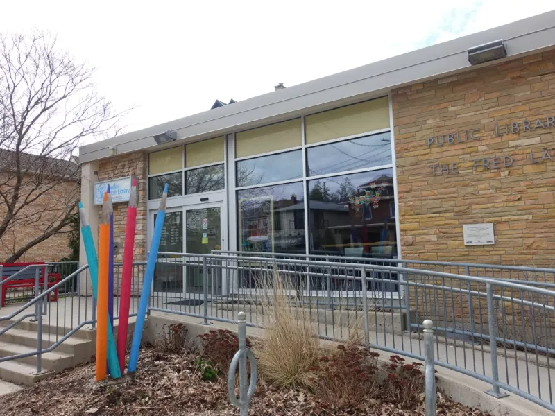 A photo of the outside of Landon Branch Library with a ramp and a large sculpture of wooden pencils in front. A red bench is in the background.