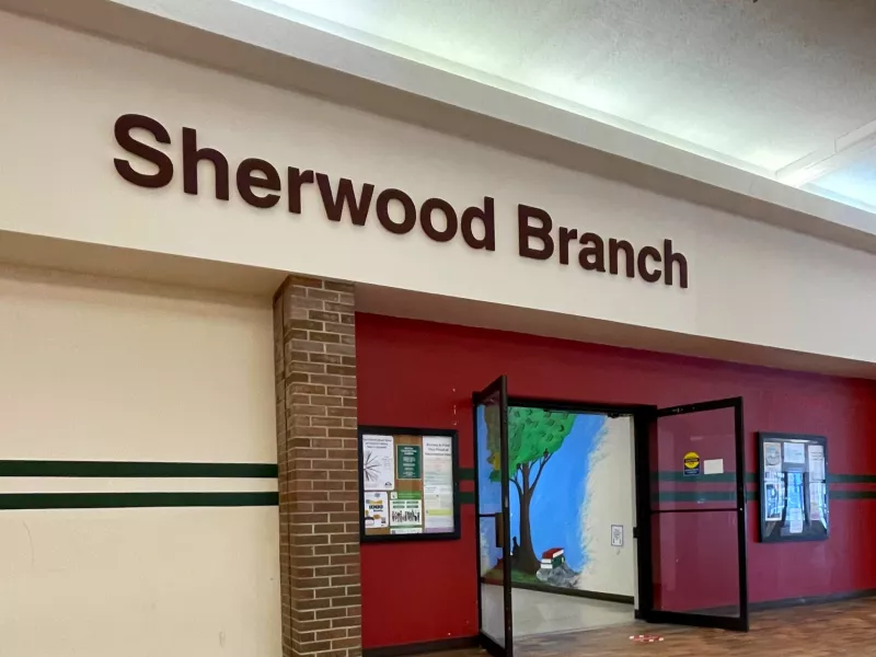 A photo of the entrance to Sherwood Branch from the Mall showing the doors open bulletin boards on both sides and a mural on the wall inside.