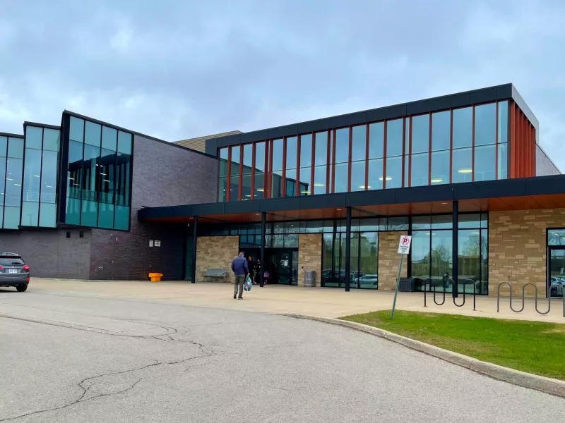 A photo of the outside of the Stoney Creek Library with a person entering and bike racks and a car out front