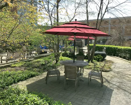 A photo of a wooden table and chairs with a red umbrella on top in the Rotary Reading Garden.